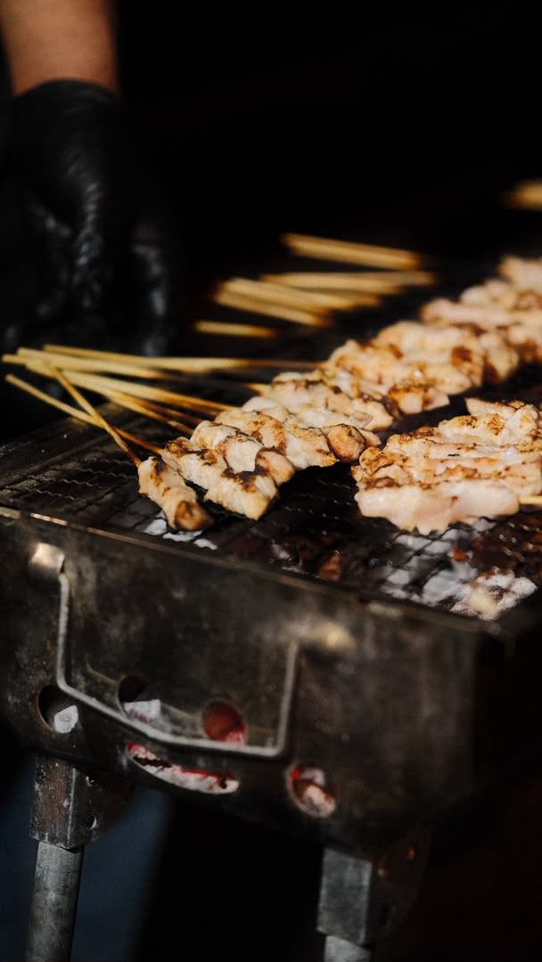 Gloved hand turning sate over the charcoal grill